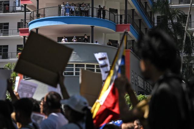 University students, opponents of the government, and relatives of political prisoners, take part in a march on the Youth Day as residents watch from balconies in Caracas on February 12, 2026. The first major opposition demonstration after the fall of Nicolas Maduro during a US military incursion a month ago gathered thousands of people in Venezuelas capital on February 12, ahead of the approval of a historic amnesty law. (Photo by Juan BARRETO / AFP)