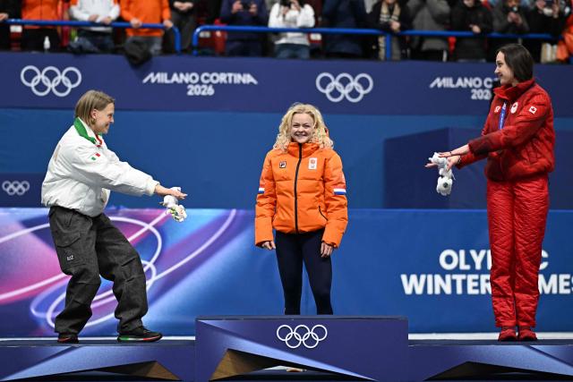 Silver medalist Italy's Arianna Fontana (L) and bronze medalist Canada's Courtney Sarault (R) gesture toward gold medalist Netherlands' Xandra Velzeboer as she arrives on the podium after competing in the short track speed skating women's 500m final during the Milano Cortina 2026 Winter Olympic Games at Milano Ice Skating Arena in Milan on February 12, 2026. (Photo by Gabriel BOUYS / AFP)