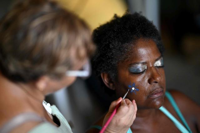 Revellers apply makeup to each other during the parade of the Loucura Suburbana (Suburban Craziness) street carnival group at the Engenho de Dentro neighborhood in Rio de Janeiro, Brazil on February 12, 2026. (Photo by Mauro PIMENTEL / AFP)