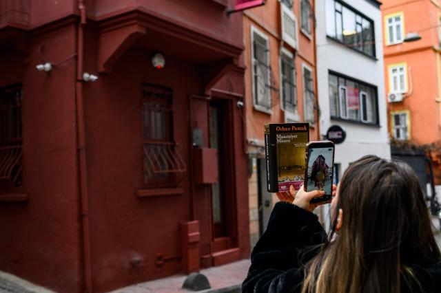 A visitor takes a photograph with The Museum of Innocence's book in front of the eponymous museum in Istanbul on February 10, 2026. On a cobbled street in Cukurcuma, a district known for its antiques shops on Istanbul's European side, the story penned by Nobel Literature Prize-winning Turkish author Orhan Pamuk has been brought to life inside the walls of a red-painted house. (Photo by Yasin AKGUL / AFP)
