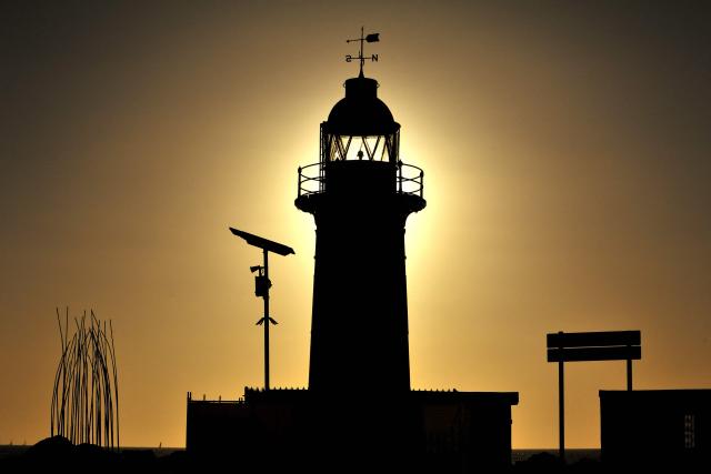 The sun sets behind a lighthouse at the entrance to Fremantle Port in Western Australia on February 11, 2026. (Photo by Antony DICKSON / AFP)