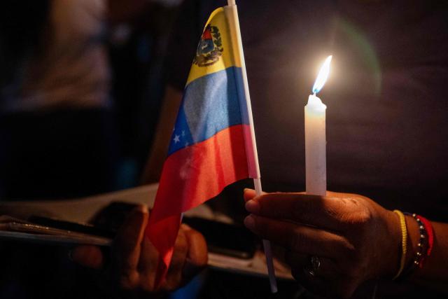 A woman holds a candle and a Venezuelan flag during a vigil of relatives of political prisoners outside El Rodeo I prison in Guatire, Miranda state, Venezuela, on February 12, 2026. Venezuela's legislature on February 12 postponed the adoption of a landmark amnesty bill expected to lead to the release of hundreds of political prisoners. (Photo by Maryorin Mendez / AFP)