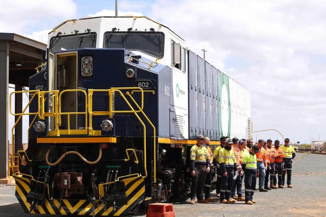 Staff members pose with a newly unveiled battery-electric locomotive by Fortescue Metals Group in Port Hedland, Western Australia on February 12, 2026. Fortescue has officially started phasing out the diesel trains that transport iron ore from its mines to port in a move that the mining group hopes will save about one million litres of diesel a year. Fortescue is aiming for its iron ore mining and transportion to emit zero carbon emissions by the end of 2030. (Photo by Antony DICKSON / AFP)