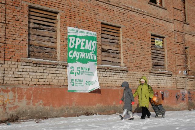 A woman and a child walk past a billboard promoting contract army service that reads "Time to serve" sitting on a building in Semiluki in the Voronezh region on January 23, 2026. (Photo by TATYANA MAKEYEVA / AFP)