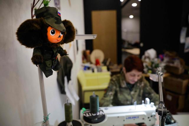 A Cheburashka toy, Soviet-era children's character, dressed in a military outfit is seen in front of Lyudmila, 64, a volunteer in an organisation sewing camouflage gear for Russian soldiers whose son went missing four months ago while fighting in Ukraine, in Voronezh on January 24, 2026. (Photo by TATYANA MAKEYEVA / AFP)