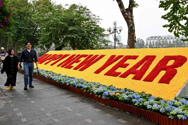 A couple walks past a Happy New Year banner ahead of the Lunar New Year in Hanoi on February 13, 2026. (Photo by Nhac NGUYEN / AFP)