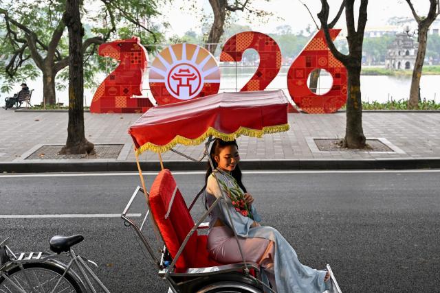 A girl poses for photos on a cyclo rickshaw near a 2026 sign ahead of the Lunar New Year at Hoan Kiem Lake in Hanoi on February 13, 2026. (Photo by Nhac NGUYEN / AFP)