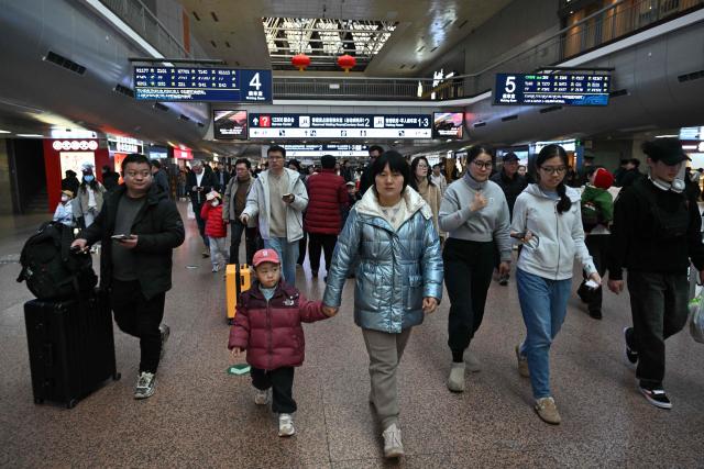Passengers walk towards gates before boarding their trains at a train station in Beijing on February 13, 2026, as people travel to their hometowns ahead of Lunar New Year celebrations. (Photo by AFP)