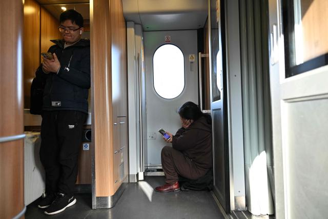 Passengers use their phones on a train in Beijing on February 13, 2026, as people travel to their hometowns ahead of Lunar New Year celebrations. (Photo by AFP)