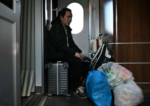 A passenger sits on a train in Beijing on February 13, 2026, as people travel to their hometowns ahead of Lunar New Year celebrations. (Photo by AFP)