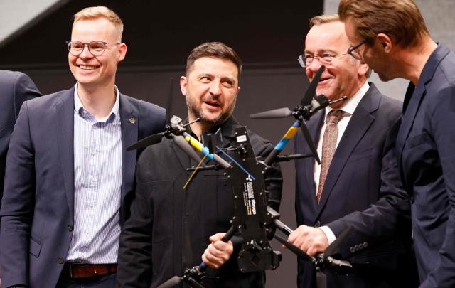 Ukrainian President Volodymyr Zelensky (2nd L) and German Defence Minister Boris Pistorius (2nd R) hold a drone as they visit the production facility of drone producing company Quantum Frontline Industries (QFI) in Gilching near Munich, southern Germany, on the sidelines of the 62nd Munich Security Conference (MSC) on February 13, 2026. Heads of state and government as well as foreign and defence ministers from all over the world are expected to attend the security policy talks from February 13 to 15, 2026. (Photo by Alexandra BEIER / AFP)