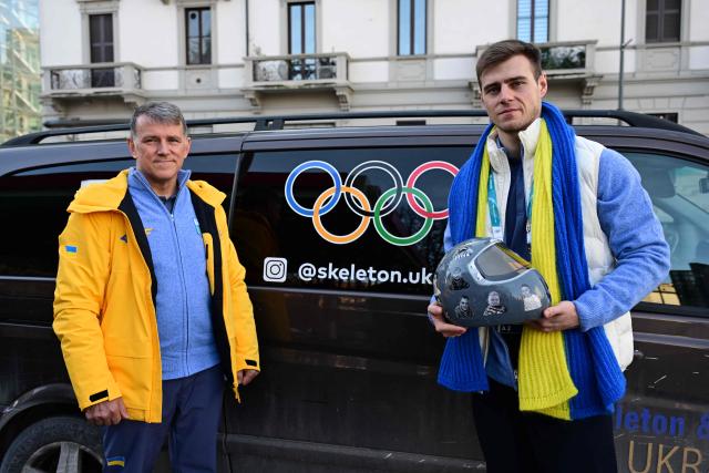 Ukrainian skeleton athlete Vladyslav Heraskevych poses with his helmet next to his father and coach, Mykhailo Heraskevych after a hearing at the Court of Arbitration for Sport (TAS) in Milan on February 13, 2026. Heraskevych was barred from the Milan-Cortina Games after refusing to back down from wearing a helmet adorned with pictures of Ukrainian sportsmen and women killed since Russian invaded in 2022. (Photo by Piero CRUCIATTI / AFP)