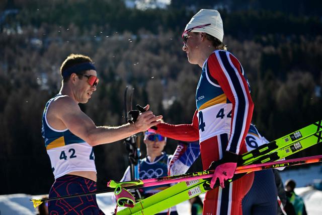 Britain's Andrew Musgrave (L) shakes hands with Norway's Johannes Hoesflot Klaebo after they crossed the finish line during the men's 10km cross-country interval start free event of the Milano Cortina 2026 Winter Olympic Games at Tesero Cross-Country Skiing Stadium in Lago di Tesero (Val di Fiemme) on February 13, 2026. (Photo by Tobias SCHWARZ / AFP)