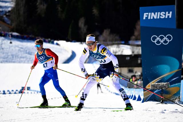 Romania's Gabriel Cojocaru (L) and Sweden's Gustaf Berglund react after crossing the finish line during the men's 10km cross-country interval start free event of the Milano Cortina 2026 Winter Olympic Games at Tesero Cross-Country Skiing Stadium in Lago di Tesero (Val di Fiemme) on February 13, 2026. (Photo by Tobias SCHWARZ / AFP)