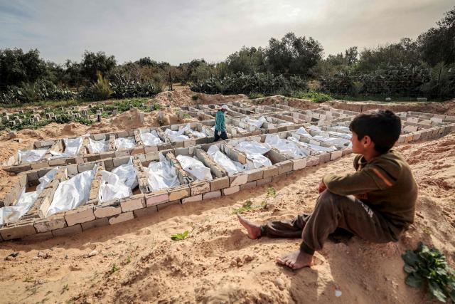 EDITORS NOTE: Graphic content / TOPSHOT - A young Palestinian boy looks on as 53 unidentified bodies are buried in a cemetery in Deir el-Balah in the central Gaza Strip on February 13, 2026. Since October 10, a fragile US-sponsored truce in Gaza has largely halted the fighting between Israeli forces and Hamas, but both sides have alleged frequent violations. (Photo by EYAD BABA / AFP)