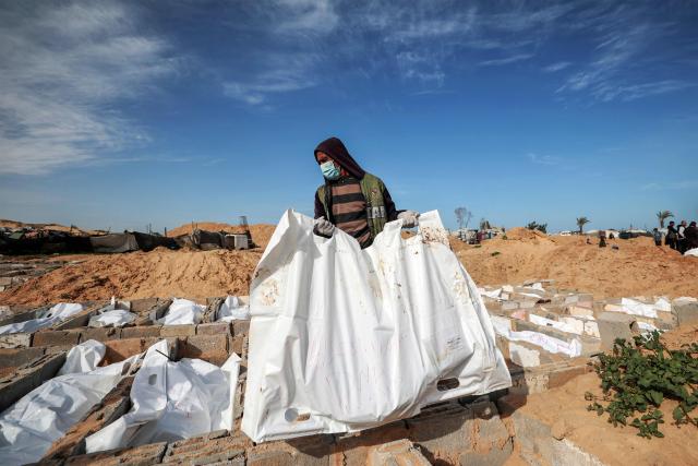 EDITORS NOTE: Graphic content / TOPSHOT - A man carries a body bag during the burial of 53 unidentified bodies at a cemetery in Deir el-Balah in the central Gaza Strip on February 13, 2026. Since October 10, a fragile US-sponsored truce in Gaza has largely halted the fighting between Israeli forces and Hamas, but both sides have alleged frequent violations. (Photo by EYAD BABA / AFP)