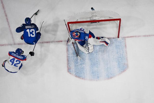 Italy's #13 Matt Bradley (C) controls the puck past Slovakia's #42 Martin Fehervary (L) and Slovakia's #31 Samuel Hlavaj (R) during the men's preliminary round Group B Ice Hockey match between Italy and Slovakia at the Milano Rho Ice Hockey Arena at the Milano Cortina 2026 Winter Olympic Games in Milan, on February 13, 2026. (Photo by JULIEN DE ROSA / AFP)