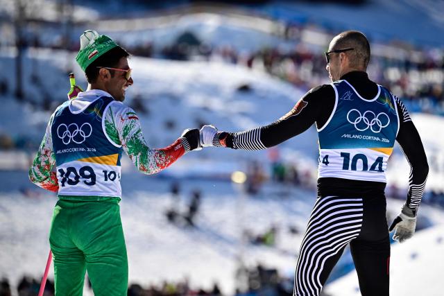 Iran's Danyal Saveh Shemshaki (L) and Mexico's Allan Corona fist bump after crossing the finish line during the men's 10km cross-country interval start free event of the Milano Cortina 2026 Winter Olympic Games at Tesero Cross-Country Skiing Stadium in Lago di Tesero (Val di Fiemme) on February 13, 2026. (Photo by Tobias SCHWARZ / AFP)