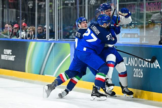 Italy's #11 Marco Zanetti (L) and Italy's #27 Thomas Larkin (R) tackle Slovakia's #20 Juraj Slafkovsky during the men's preliminary round Group B Ice Hockey match between Italy and Slovakia at the Milano Rho Ice Hockey Arena at the Milano Cortina 2026 Winter Olympic Games in Milan, on February 13, 2026. (Photo by JULIEN DE ROSA / AFP)