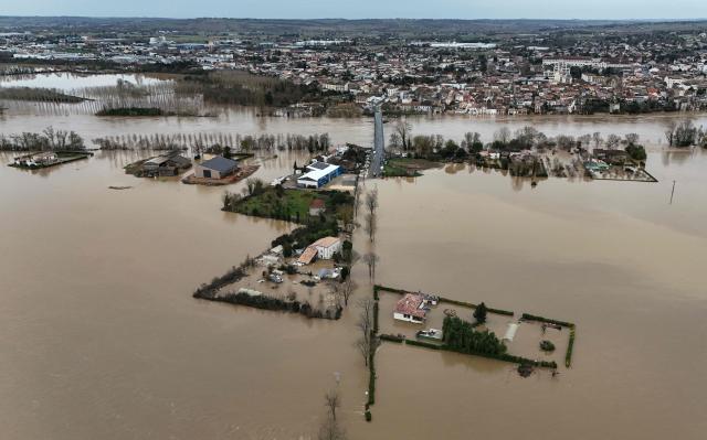 This aerial photograph shows the overflowing Garonne river inundating a residential area in Tonneins, south-western France on February 13, 2026, after winds of Storm Nils swept across France. Storm Nils, which swept across France for two days, has claimed a second life according to the government in the south-west, where a red alert remains in place for flooding on the Garonne river. France's government spokesperson announced on the morning of February 13, 2026, on French TV channel TF1 the death of a man who was "on a ladder in his garden" in Tarn-et-Garonne. (Photo by Christophe ARCHAMBAULT / AFP)