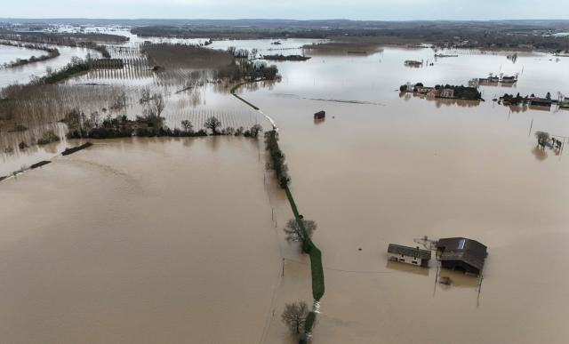 This aerial photograph shows the overflowing Garonne river inundating a residential area in Tonneins, south-western France on February 13, 2026, after winds of Storm Nils swept across France. Storm Nils, which swept across France for two days, has claimed a second life according to the government in the south-west, where a red alert remains in place for flooding on the Garonne river. France's government spokesperson announced on the morning of February 13, 2026, on French TV channel TF1 the death of a man who was "on a ladder in his garden" in Tarn-et-Garonne. (Photo by Christophe ARCHAMBAULT / AFP)