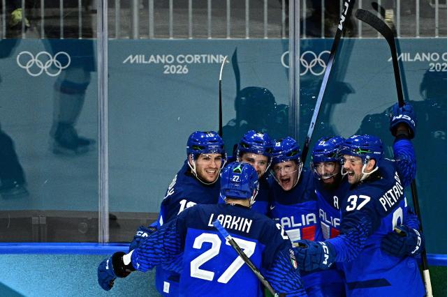 Italy's #10 Dustin James Gazley (C) celebrates with teammates after scoring his team second goal during the men's preliminary round Group B Ice Hockey match between Italy and Slovakia at the Milano Rho Ice Hockey Arena at the Milano Cortina 2026 Winter Olympic Games in Milan, on February 13, 2026. (Photo by JULIEN DE ROSA / AFP)