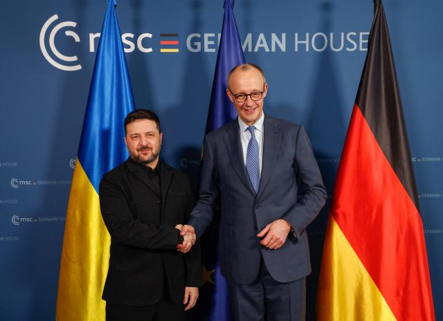Ukrainian President Volodymyr Zelensky (L) and German Chancellor Friedrich Merz shake hands prior bilateral talks during the 62nd Munich Security Conference (MSC) on February 13, 2026 in Munich, southern Germany. Heads of state and government as well as foreign and defence ministers from all over the world are expected to attend the security policy talks from February 13 to 15, 2026. (Photo by Michaela STACHE / POOL / AFP)