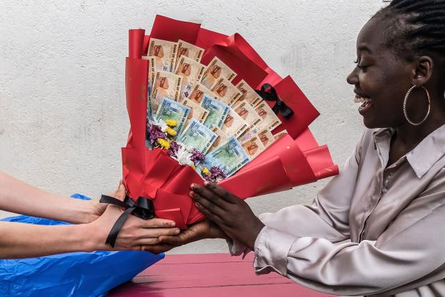 (FILES) A woman reacts as she receives a bouquet made of banknotes and flowers from her boyfriend as a surprise ahead of Valentine’s Day during a hangout in Kampala on February 7, 2026. In the run-up to this year's Valentine's Day on February 14, 2026, romantics from Paris to Lagos and in the ongoing Olympic Games, are preparing to celebrate the Roman Saint Valentine whose feast day has since the Middle Ages been associated with courting couples. (Photo by Badru Katumba / AFP)
