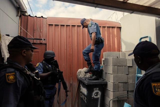 TOPSHOT - South African policemen search a house during the crime prevention operation Shanela in Tafelsig, Cape Town on February 13, 2026. Operation Shanela, "to sweep" in Setswana, is a high-density, multi-disciplinary, and countrywide crime-fighting initiative led by the South African Police Service (SAPS) to combat serious crime, specifically targeting hotspots, illegal mining, and unlicensed firearms. (Photo by GIANLUIGI GUERCIA / AFP)