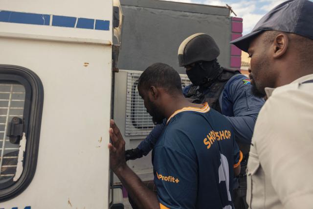 A South African policeman detains an alleged illegal immigrant during the crime prevention operation Shanela in Tafelsig, Cape Town on February 13, 2026. Operation Shanela, "to sweep" in Setswana, is a high-density, multi-disciplinary, and countrywide crime-fighting initiative led by the South African Police Service (SAPS) to combat serious crime, specifically targeting hotspots, illegal mining, and unlicensed firearms. (Photo by GIANLUIGI GUERCIA / AFP)