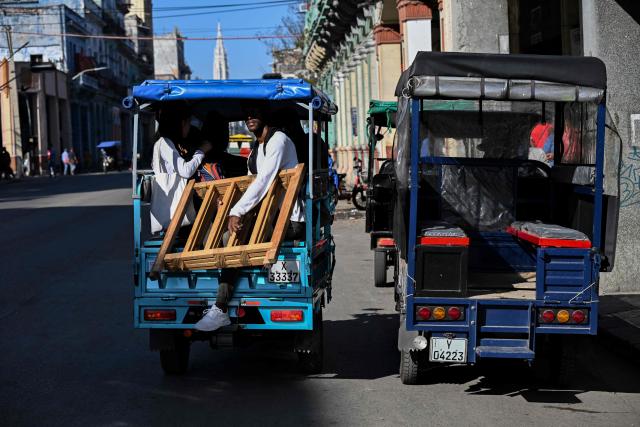 People ride an electric tricycle as another is parked on a street in Havana on February 13, 2026. The fuel crisis in Cuba, and particularly in Havana, is forcing many workers who depend on daily mobility to abandon gasoline cars and turn to electric tricycles and bicycle taxis as more accessible alternatives. (Photo by YAMIL LAGE / AFP)