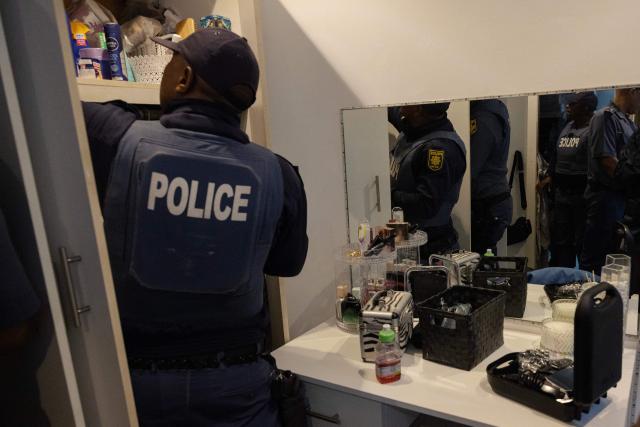 South African policemen search a house during the crime prevention operation Shanela in Tafelsig, Cape Town on February 13, 2026. Operation Shanela, "to sweep" in Setswana, is a high-density, multi-disciplinary, and countrywide crime-fighting initiative led by the South African Police Service (SAPS) to combat serious crime, specifically targeting hotspots, illegal mining, and unlicensed firearms. (Photo by GIANLUIGI GUERCIA / AFP)