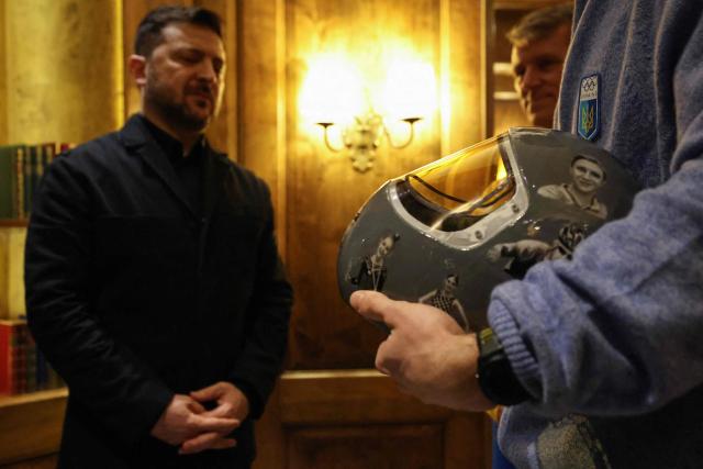 Ukrainian skeleton athlete Vladyslav Heraskevych (R) presents his helmet to Ukrainian President Volodymyr Zelensky in Munich, southern Germany, on the sidelines of the 62nd Munich Security Conference (MSC) on February 13, 2026. Heraskevych was barred from the Milan-Cortina Games after refusing to back down from wearing a helmet adorned with pictures of Ukrainian sportsmen and women killed since Russian invaded in 2022. (Photo by Alexandra BEIER / AFP)
