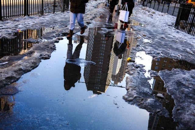 People walk through puddles and melting snow on a sidewalk on the Upper West Side of the Manhattan borough of New York City on February 13, 2026. (Photo by CHARLY TRIBALLEAU / AFP)