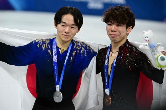 Silver medallist Japan's Yuma Kagiyama (L) and bronze medallist Japan's Shun Sato (R) pose with flags of their country following the victory ceremony of the figure skating men's singles free skating final during the Milano Cortina 2026 Winter Olympic Games at Milano Ice Skating Arena in Milan on February 13, 2026. (Photo by Piero CRUCIATTI / AFP)