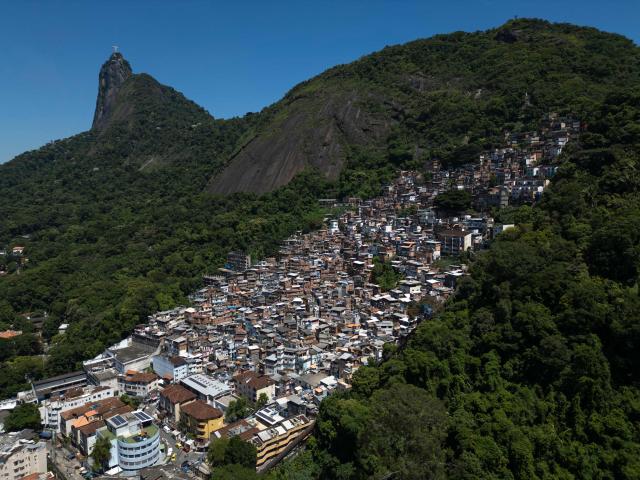 This aerial view shows the Santa Marta favela (R) and the Christ the Redeemer statue on the top of Corcovado mountain (L) in the south zone of Rio de Janeiro, Brazil, on February 13, 2026. The Santa Marta favela, located on Dona Marta Hill between Botafogo and Laranjeiras in Rio de Janeiro's South Zone, is a vibrant community of roughly 3,9006,000 residents. It is a popular, generally safe tourist destination famous for its steep terrain, colorful houses, and the Michael Jackson statue marking where his 1995 music video was filmed. (Photo by MAURO PIMENTEL / AFP)