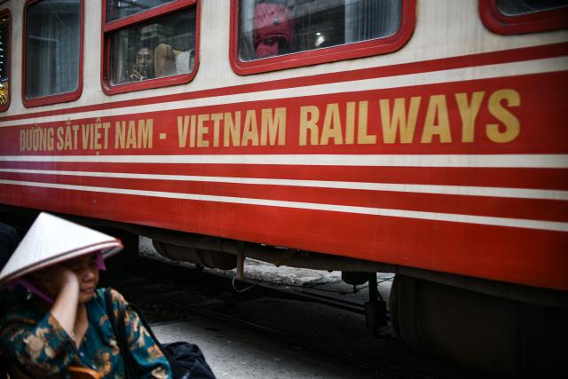 A street vendor sits as a train passes on a railway track on the popular train street in Hanoi on February 13, 2026. (Photo by Amaury PAUL / AFP)