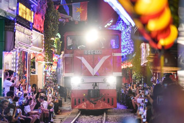 TOPSHOT - Tourists take photos as a train passes along the railway track on the popular train street in Hanoi on February 13, 2026. (Photo by Amaury PAUL / AFP)