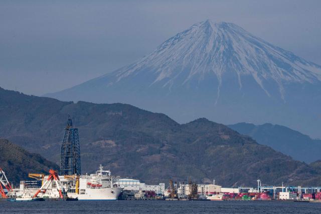 Japan's deep-sea drilling vessel Chikyu (bottom L) is seen docked at Shimizu port as Mount Fuji looms in the background, in Shimizu, Shizuoka prefecture on February 14, 2026. (Photo by Yuichi YAMAZAKI / AFP)