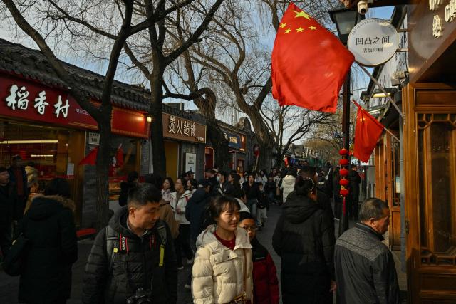 China’s national flags are seen as people walk at a market in Beijing on February 14, 2026, ahead of the Lunar New Year of the Horse. (Photo by ADEK BERRY / AFP)