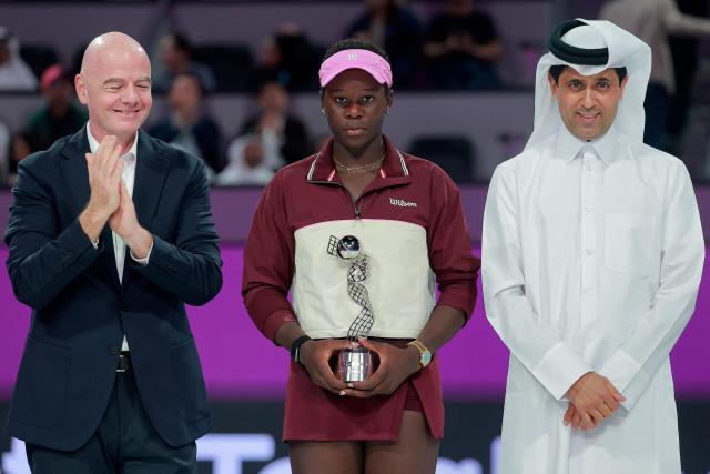 Canada's Victoria Mboko (C) holds the runners-up trophy as she stands in between International Association Football Federation (FIFA) President Gianni Infantino (L) and French football club Paris Saint-Germain's Qatari president Nasser al-Khelaifi, after loosing to Czech Republic's Karolina Muchova in the women’s singles final match, at the Qatar Open tennis tournament in Doha on February 14, 2026. (Photo by Karim JAAFAR / AFP)