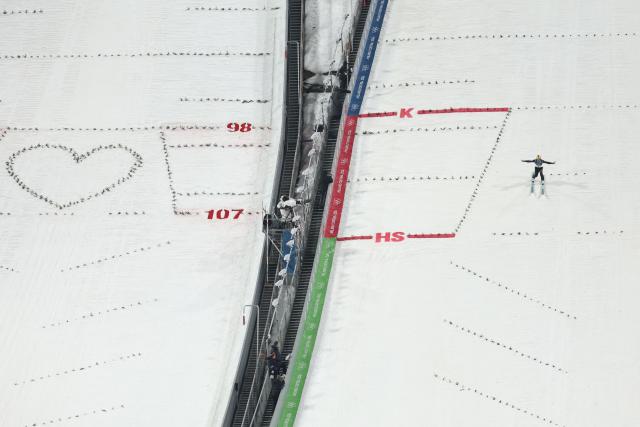 Italy's Francesco Cecon lands after a jump next to a heart shape on the adjacent slope during the trial round of the men's large hill individual ski jumping of the Milano Cortina 2026 Winter Olympic Games at Predazzo Ski Jumping Stadium in Predazzo (Val di Fiemme), on February 14, 2026. (Photo by Anne-Christine POUJOULAT / AFP)