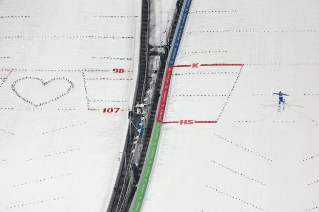 Turkey's Muhammed Ali Bedir lands after a jump next to a heart shape on the adjacent slope during the trial round of the men's large hill individual ski jumping of the Milano Cortina 2026 Winter Olympic Games at Predazzo Ski Jumping Stadium in Predazzo (Val di Fiemme), on February 14, 2026. (Photo by Anne-Christine POUJOULAT / AFP)
