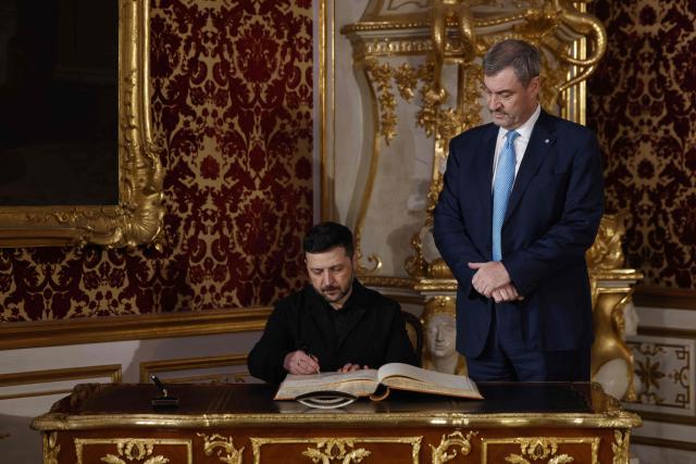 Bavarian State Premier Markus Soeder (R) looks on as Ukrainian President Volodymyr Zelensky signs the guest book at the Munich Residence palace, prior to the traditional dinner on the occasion of the Munich Security Conference (MSC), on February 14, 2026 in Munich, southern Germany. (Photo by Michaela STACHE / AFP)
