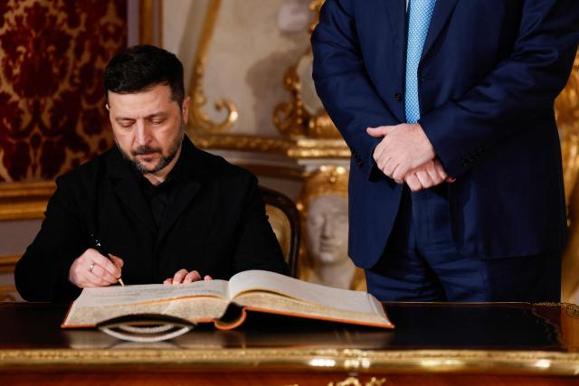 Bavarian State Premier Markus Soeder (R) looks on as Ukrainian President Volodymyr Zelensky signs the guest book at the Munich Residence palace, prior to the traditional dinner on the occasion of the Munich Security Conference (MSC), on February 14, 2026 in Munich, southern Germany. (Photo by Michaela STACHE / AFP)