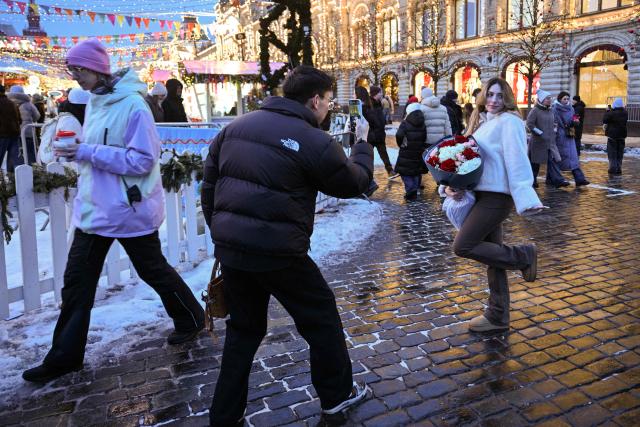 A woman poses for pictures with a bouquet of flowers on Red Square in central Moscow on February 14, 2026. (Photo by HECTOR RETAMAL / AFP)