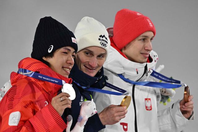 (From L) Silver medallist Japan's Ren Nikaido, gold medallist Slovenia's Domen Prevc and bronze medallist Poland's Kacper Tomasiak celebrate on the podium of the men's large hill individual ski jumping of the Milano Cortina 2026 Winter Olympic Games at Predazzo Ski Jumping Stadium in Predazzo (Val di Fiemme), on February 14, 2026. (Photo by Javier SORIANO / AFP)
