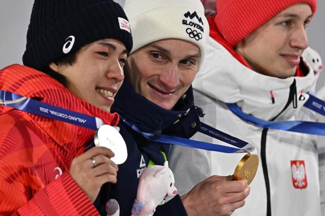 (From L) Silver medallist Japan's Ren Nikaido, gold medallist Slovenia's Domen Prevc and bronze medallist Poland's Kacper Tomasiak celebrate on the podium of the men's large hill individual ski jumping of the Milano Cortina 2026 Winter Olympic Games at Predazzo Ski Jumping Stadium in Predazzo (Val di Fiemme), on February 14, 2026. (Photo by Javier SORIANO / AFP)