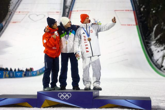(From L) Silver medallist Japan's Ren Nikaido, gold medallist Slovenia's Domen Prevc and bronze medallist Poland's Kacper Tomasiak celebrate on the podium of the men's large hill individual ski jumping of the Milano Cortina 2026 Winter Olympic Games at Predazzo Ski Jumping Stadium in Predazzo (Val di Fiemme), on February 14, 2026. (Photo by Anne-Christine POUJOULAT / AFP)