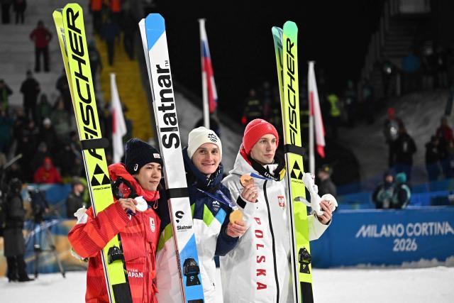 (From L) Silver medallist Japan's Ren Nikaido, gold medallist Slovenia's Domen Prevc and bronze medallist Poland's Kacper Tomasiak celebrate on the podium of the men's large hill individual ski jumping of the Milano Cortina 2026 Winter Olympic Games at Predazzo Ski Jumping Stadium in Predazzo (Val di Fiemme), on February 14, 2026. (Photo by Javier SORIANO / AFP)